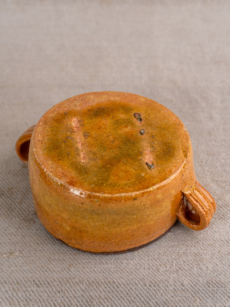 Compact round French Vallauris glazed terracotta pot with dual handles, upside down on gray textured surface.