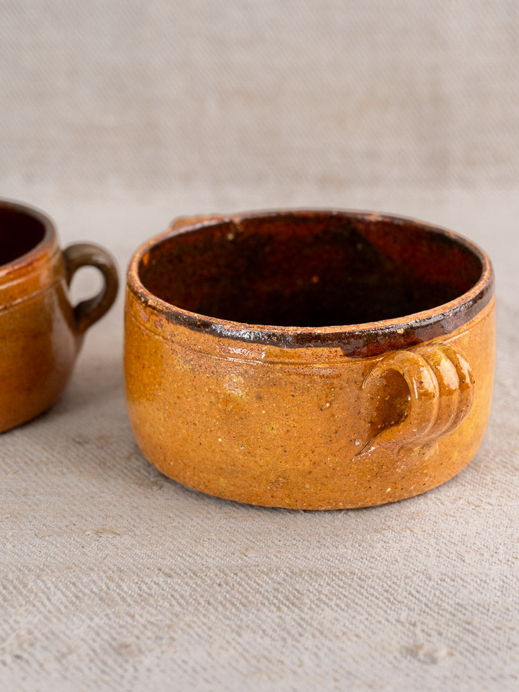 Set of three antique French Vallauris terracotta pots with side handles and rustic brown glaze, displayed on a neutral textured surface.