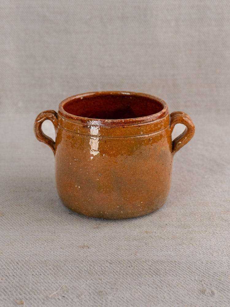 Small French Vallauris glazed terracotta pot with two handles on textured neutral fabric.