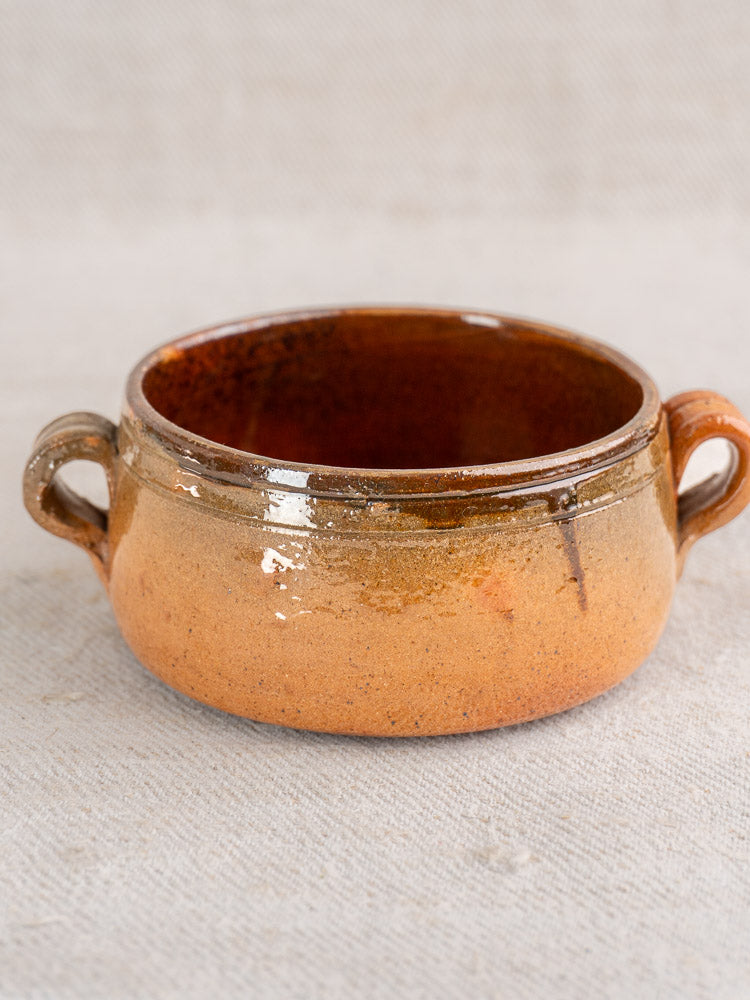 Antique French Vallauris glazed terracotta pot with round form and twin handles on neutral fabric.