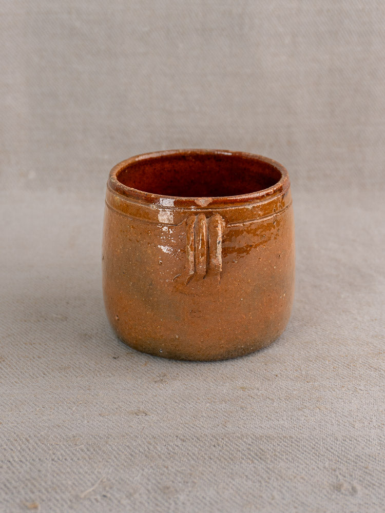 Trio of antique French Vallauris pots with rich brown glaze on light gray textured fabric background.