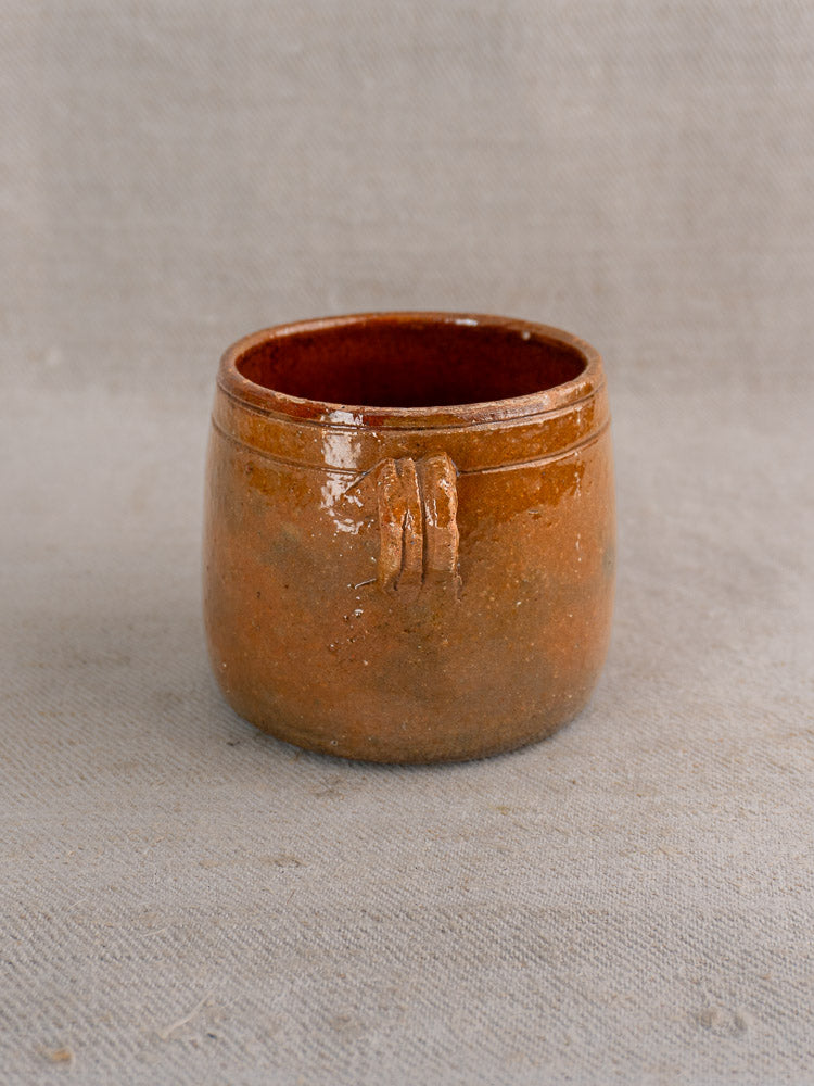 Antique French Vallauris glazed terracotta pot with rich brown glaze and decorative ridge on gray fabric.