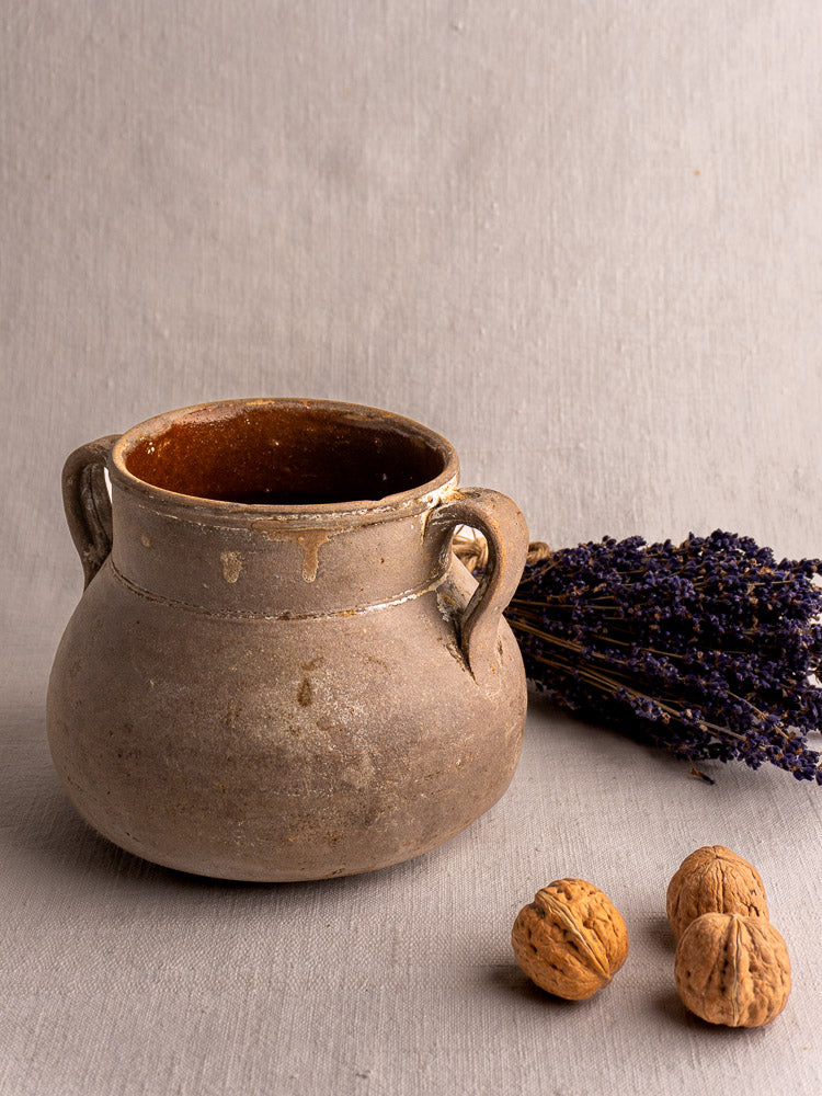 Antique French Toupin earthenware two-handle pot on light fabric with dried lavender and whole walnuts.