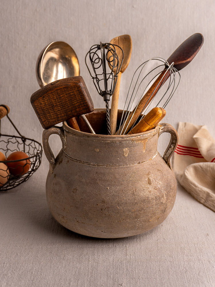 Antique French Toupin earthenware pot with utensils, beside a wire basket of brown eggs on red-striped cloth.