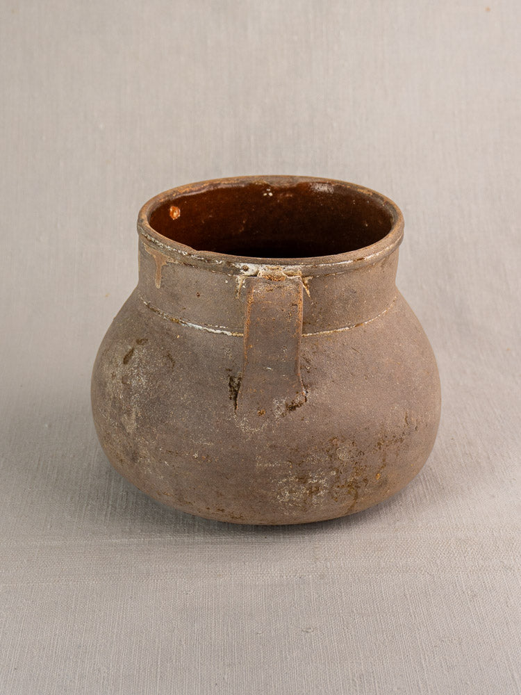 Antique French toupin earthenware cooking pot with two handles on a light gray textured surface.