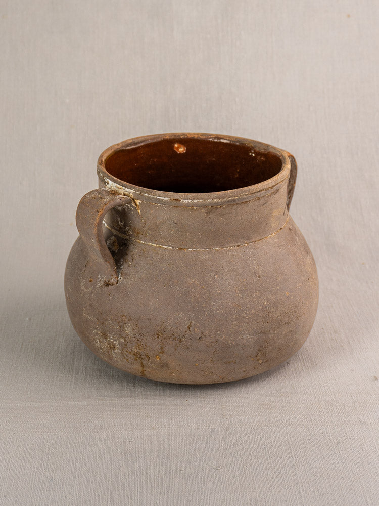 Antique French toupin earthenware two-handle cooking pot with rustic brown matte glaze on a light gray surface.