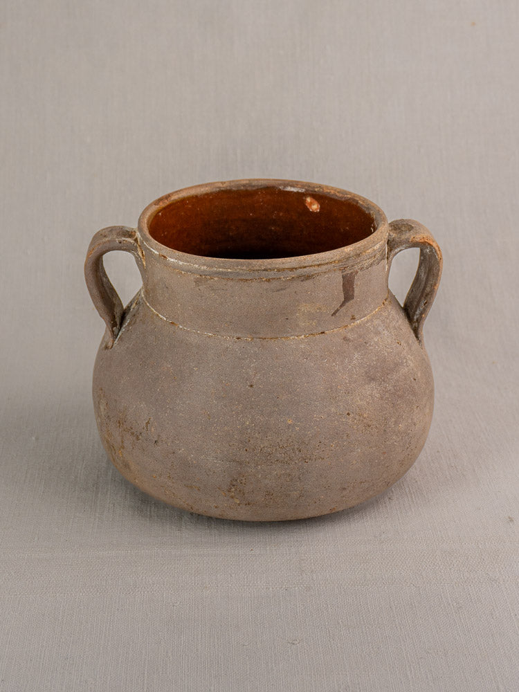 Antique French Toupin, round brown earthenware pot with two handles and wide opening on a neutral gray background.