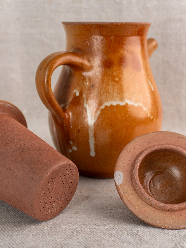 Mid-century French stoneware coffee pot with two handles, clay lid, and infuser on beige textured fabric.