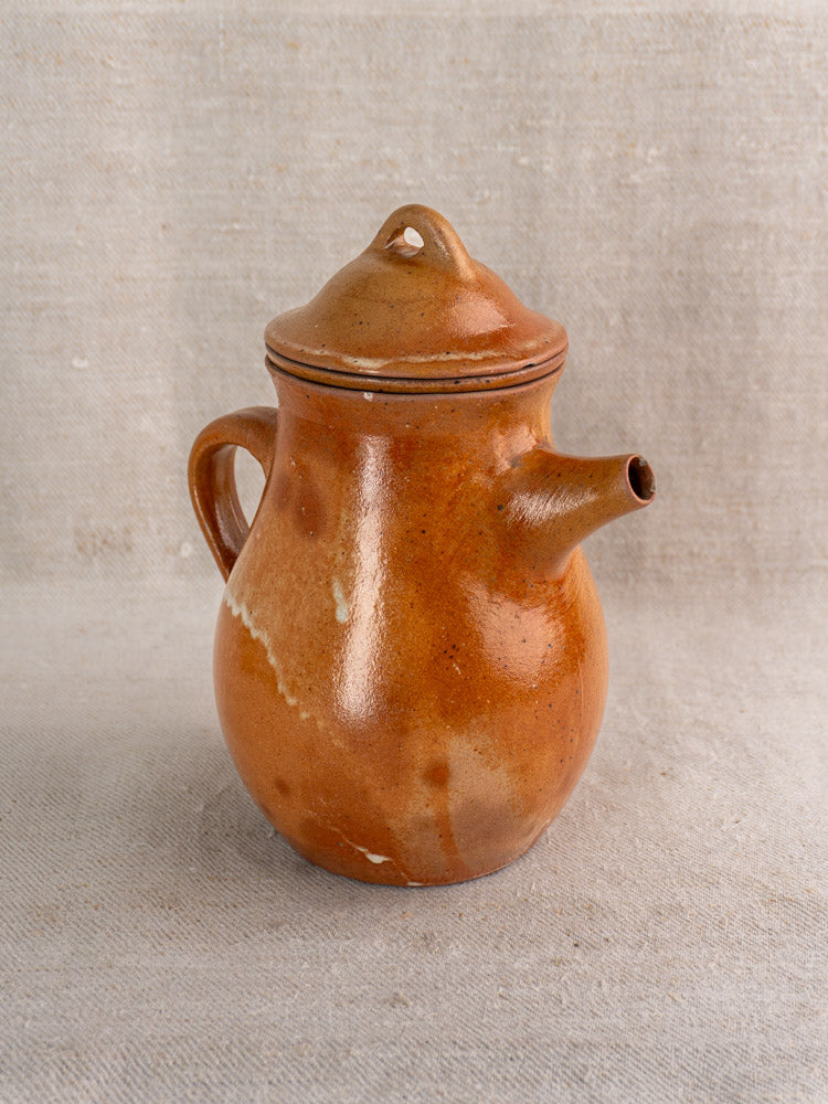 Mid-century French salt-glazed stoneware coffee pot with infuser, lid, and curved handle on fabric surface.