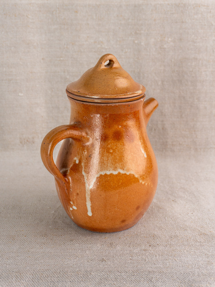 Antique French stoneware coffee pot with lid, handle, and salt-glazed Grès finish on textured beige fabric.