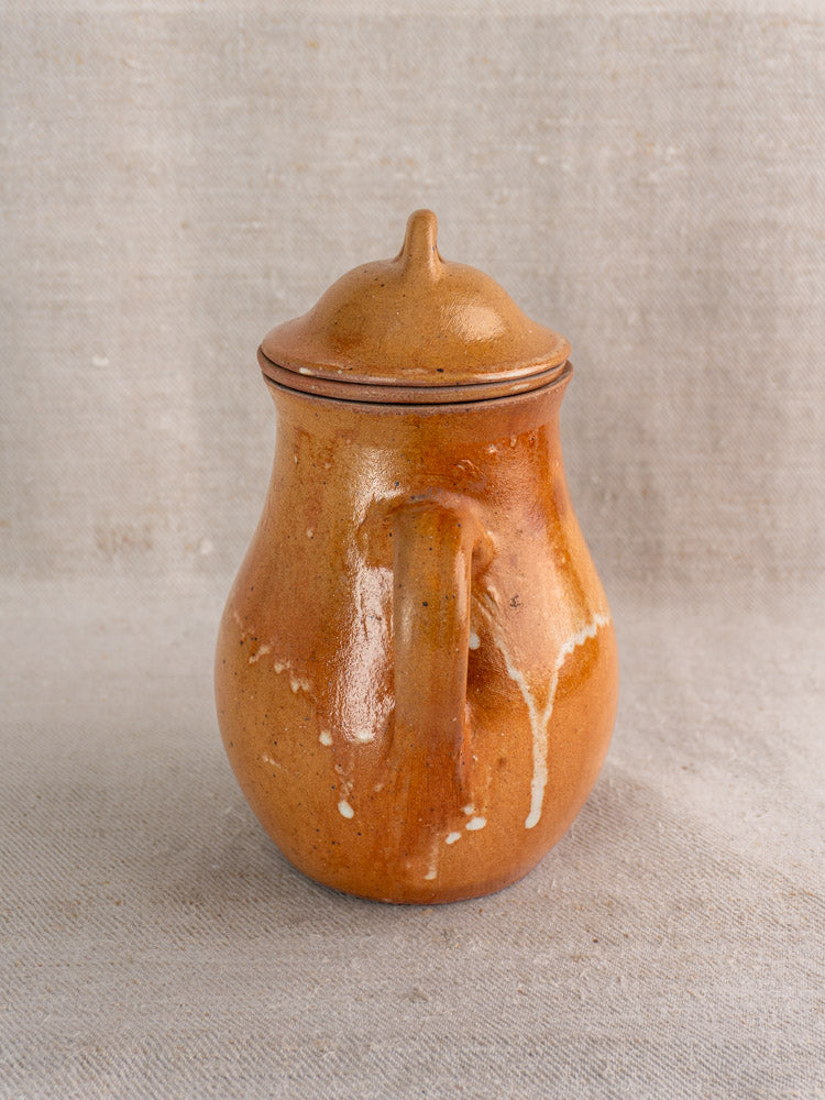 Mid-century French stoneware coffee pot with infuser, glossy brown glaze, white drips, on neutral textured fabric.