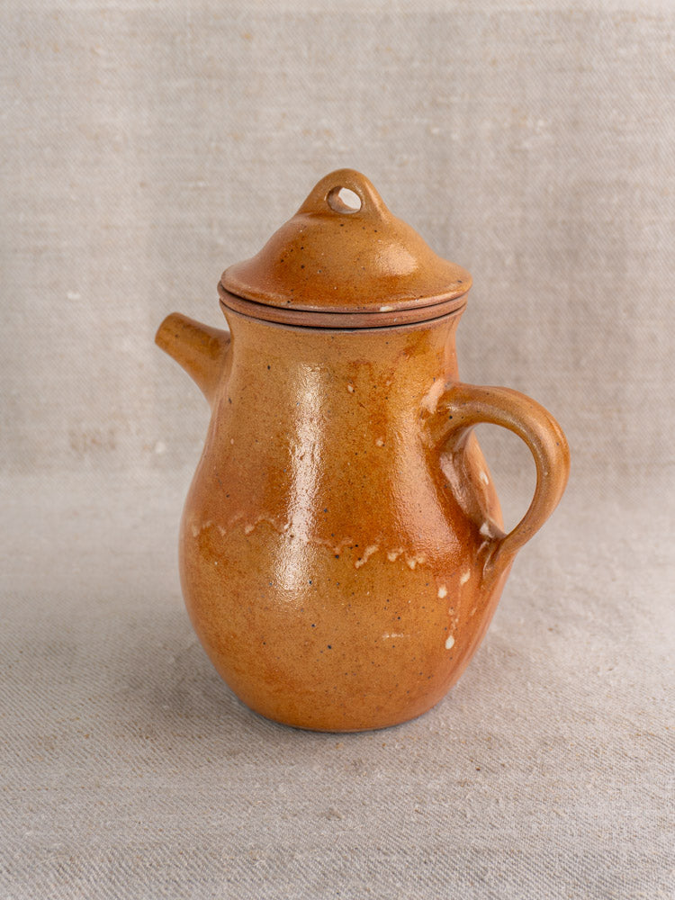 Antique French stoneware coffee pot in brown salt-glazed grès with infuser, on light textured fabric background.