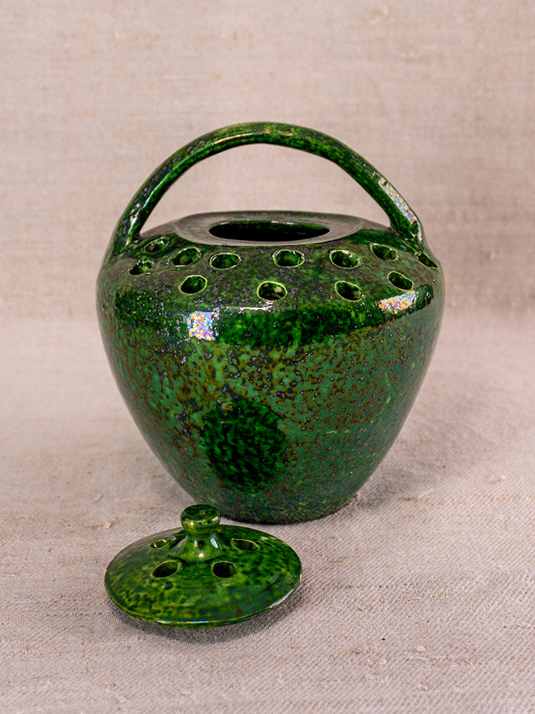 Mid-20th century French Vallauris green glazed ceramic chaufferette with handle and lid on beige fabric background.