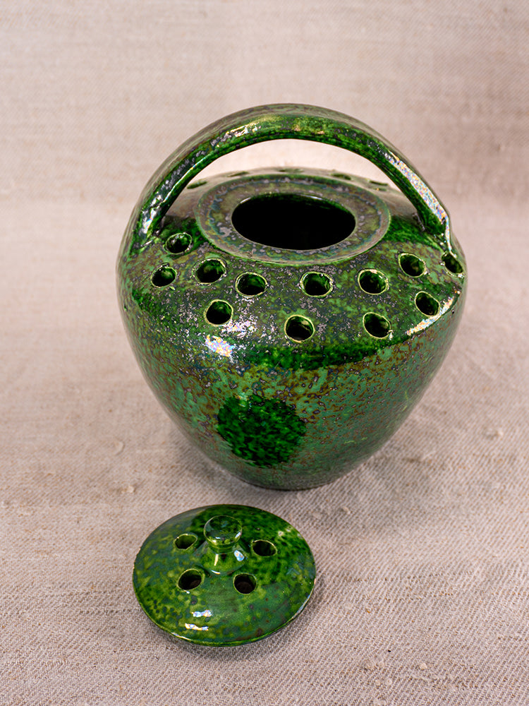 Antique French Vallauris green glazed ember warmer with round body, curved handle, and vented lid on beige surface.