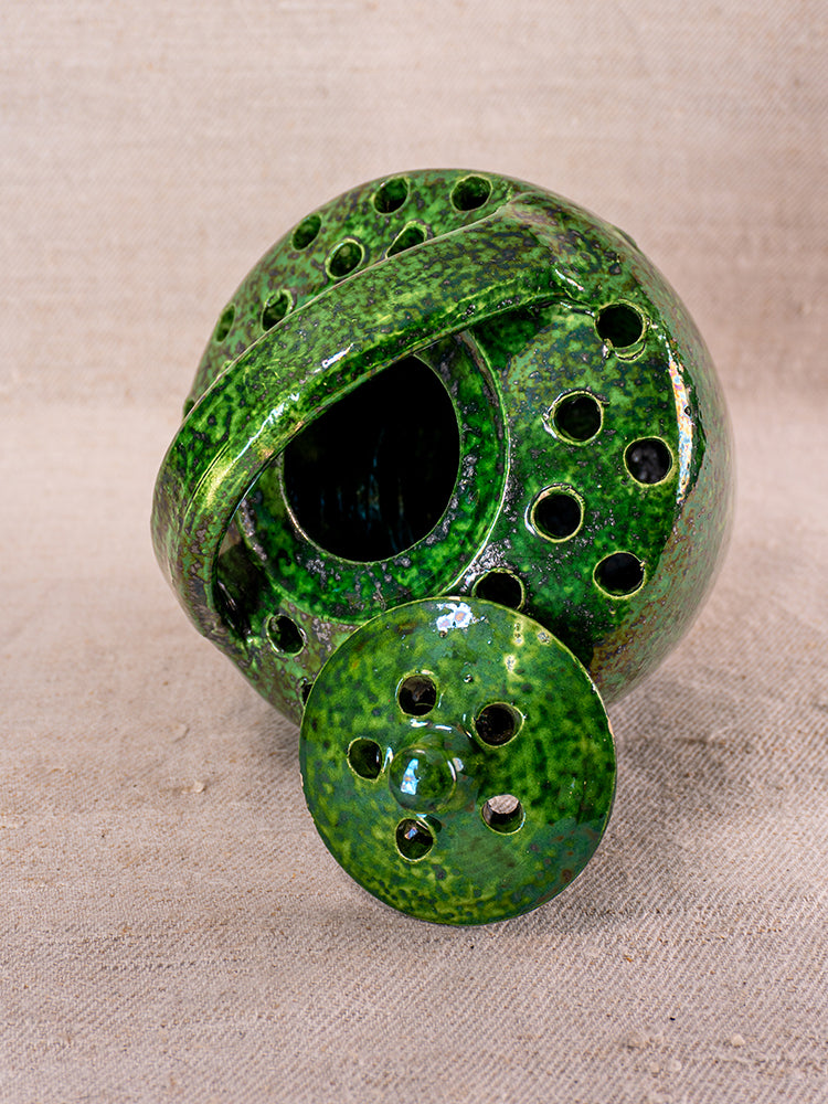 Mid-century French Vallauris green-glazed ceramic chaufferette with perforated lid on beige fabric.