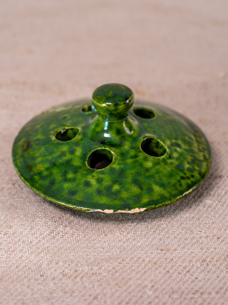 Antique French Vallauris green glazed chaufferette with knob handle, rim chipping, on beige textured fabric.