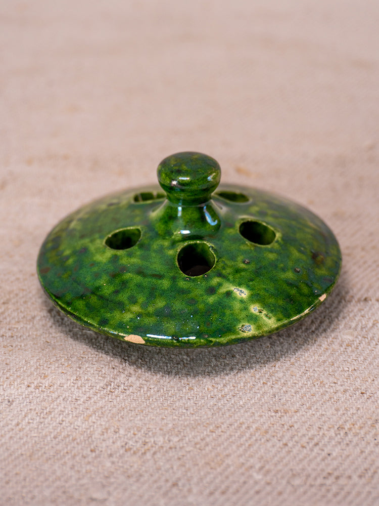 Antique French Vallauris green-glazed ceramic chaufferette lid with knob and vent holes on textured beige surface.