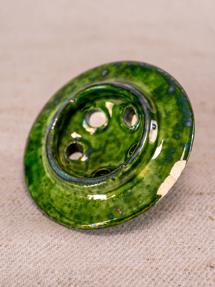 Antique French Vallauris green-glazed ceramic chaufferette with slight edge chip on beige textured fabric background.