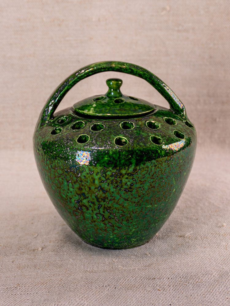 Antique French Vallauris green glazed chaufferette with handle, lid, and vent holes on neutral fabric background.