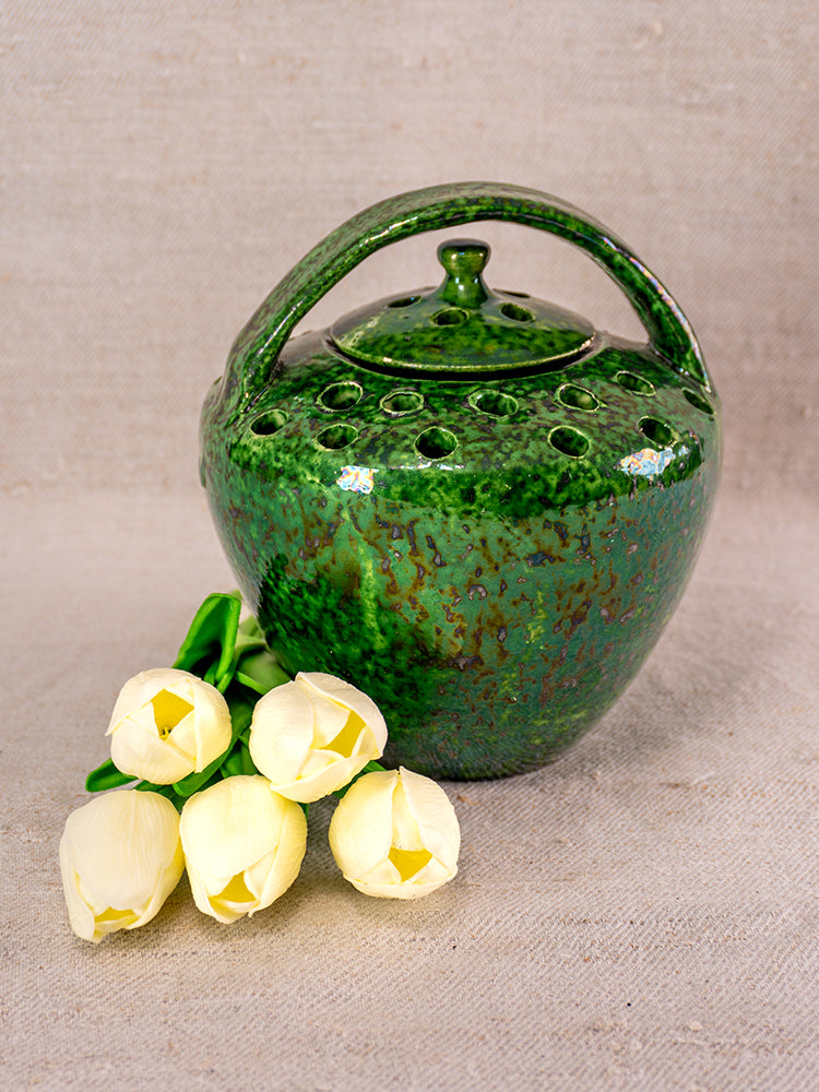 Mid-20th century French Vallauris green glazed chaufferette with handle and lid on beige fabric beside white tulips.