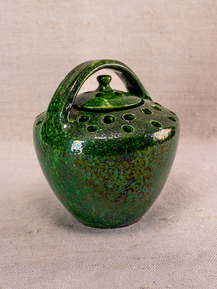 Antique French Vallauris green glazed chaufferette with pierced lidded top and arched handle on neutral textured surface.