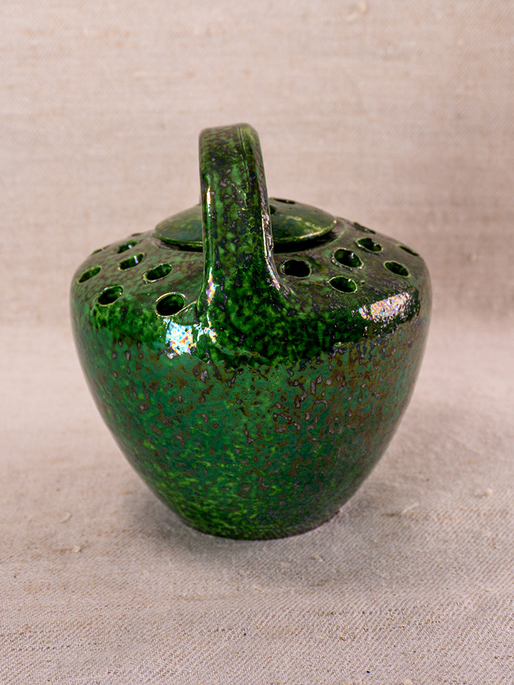 Mid-20th century French Vallauris green glazed ceramic chaufferette with handle, speckled finish, on neutral fabric background.