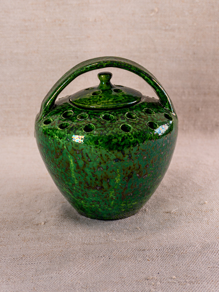 Mid-20th century French Vallauris green glazed chaufferette with handle, lid, and vent holes on textured beige fabric.