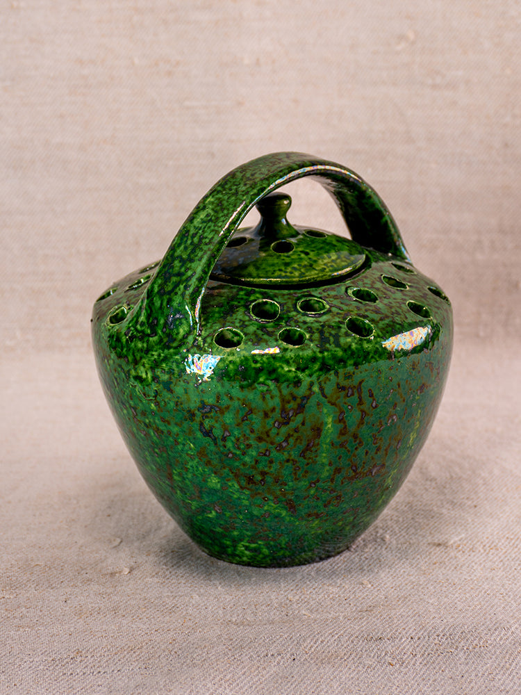 Antique French Vallauris green glazed chaufferette with arched handle and vented lid on beige fabric.