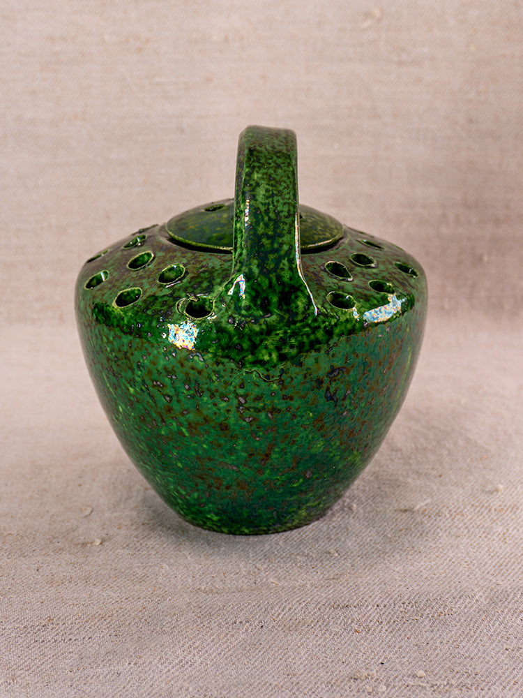 Antique French Vallauris green glazed ember warmer with handle and vent holes on neutral woven fabric background.