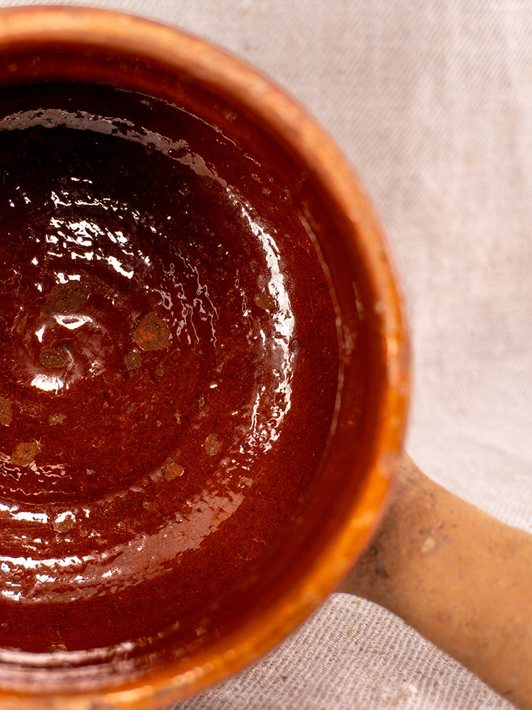 Vallauris glazed terracotta Pot à Lait stamped Societe Generale, shiny interior, earthy handle on beige textured fabric.