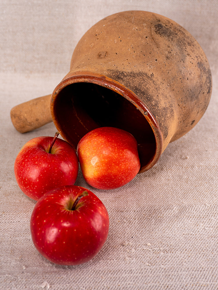 Glazed terracotta Vallauris Pot à Lait, Societe Generale stamp, with apples on beige fabric surface.