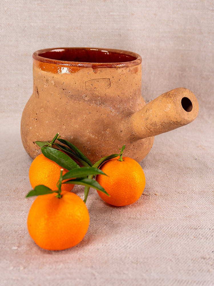 Vallauris terracotta Pot à Lait with Societe Generale stamp, rustic side handle, textured glaze on neutral fabric background.