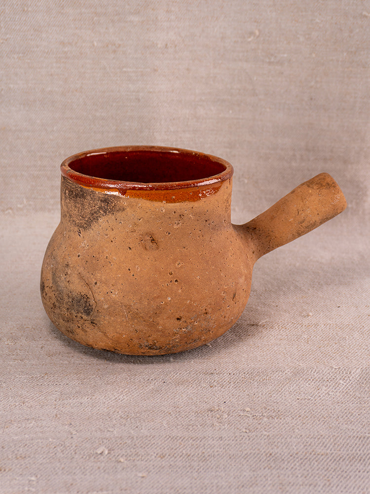 Vallauris terracotta Pot à Lait with Societe Generale stamp, rustic side handle, textured glaze on neutral fabric background.