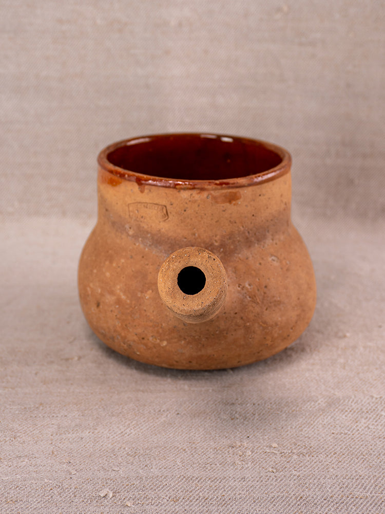 Tan glazed Vallauris Pot à Lait in terracotta, Societe Generale stamp, reddish-brown interior, on beige fabric.