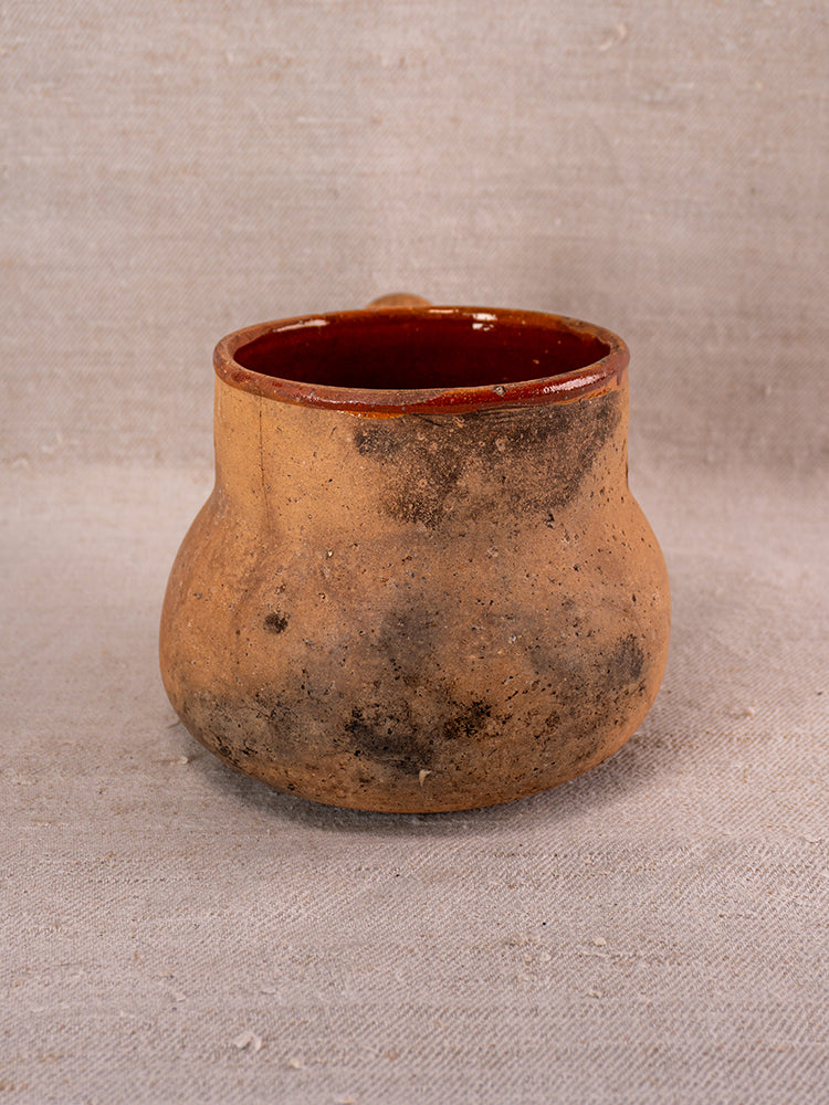 Vallauris Pot à Lait in glazed terracotta with Societe Generale stamp, rustic unglazed exterior, on neutral fabric.