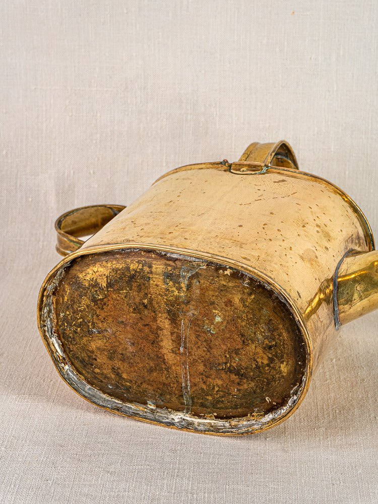 Antique French brass watering can with hinged lid and curved handles, circa 1900, on neutral background.