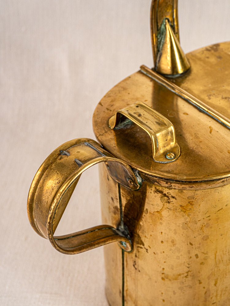 Antique French brass watering can with hinged lid, curved handle, patina, and riveted aged finish.