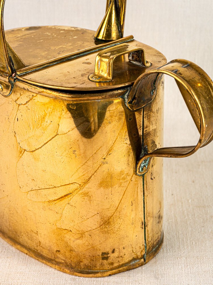 Antique French brass watering can circa 1900 with hinged lid, curved handle, patina on neutral fabric.