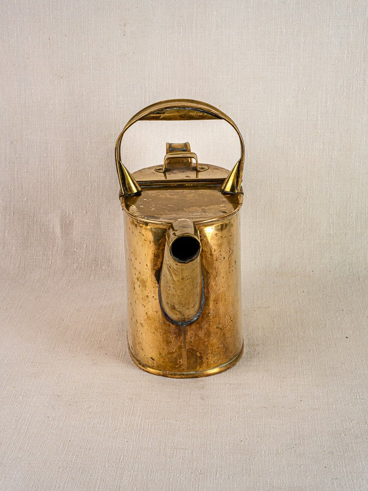 Antique French brass watering can with hinged lid, large handle and spout on fabric background.