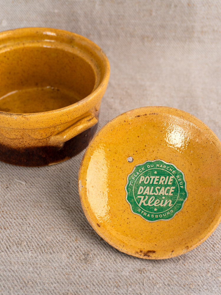 Antique French Klein Strasbourg cocotte in rustic yellow-brown glazed earthenware on textured beige fabric.
