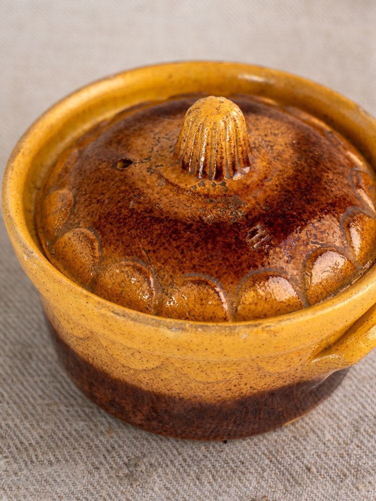 Antique French glazed earthenware cocotte by Klein Strasbourg in brown and yellow on textured beige fabric background.