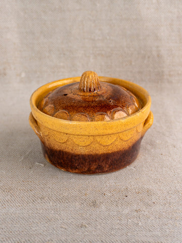 Antique French Alsace glazed earthenware cocotte by Klein Strasbourg with lid on textured beige fabric.