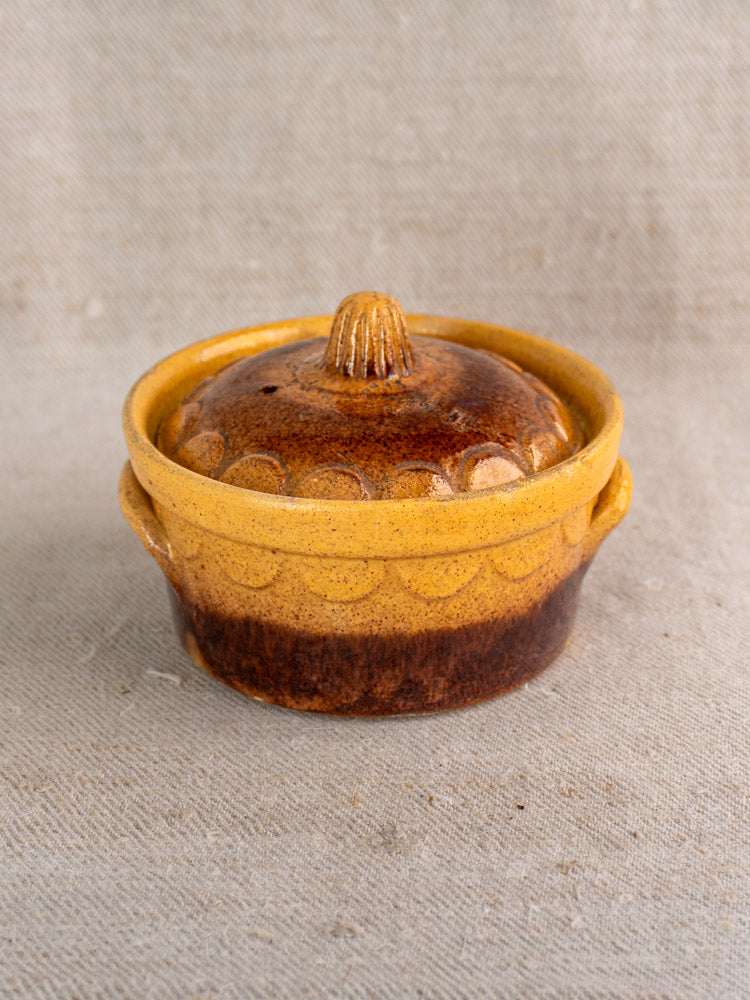 Antique French Alsace glazed earthenware cocotte by Klein Strasbourg with lid on textured beige fabric.