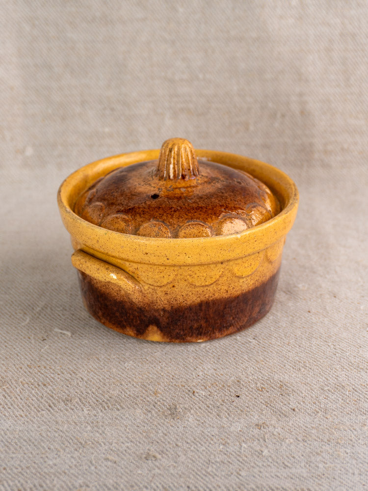 Antique French Klein Strasbourg glazed earthenware cocotte with round shape and knobbed lid on beige textured fabric background.