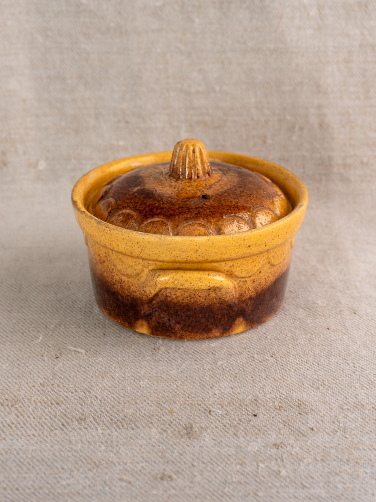 Antique French earthenware cocotte by Klein Strasbourg, amber brown glaze, ridged lid, on neutral linen background.
