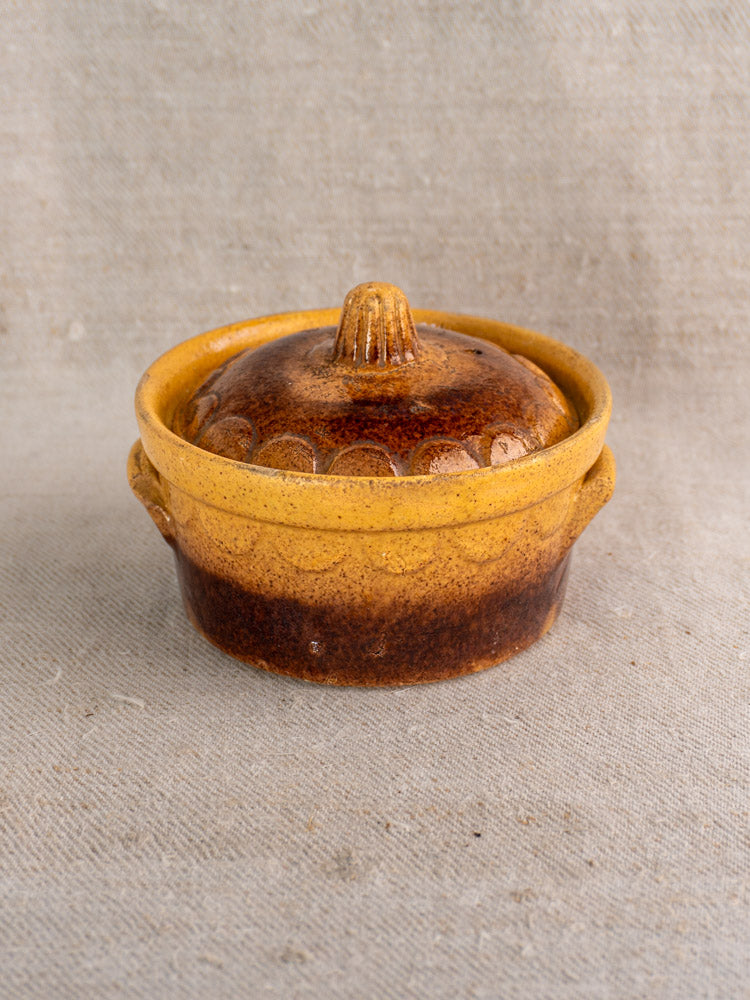 Antique French cocotte, Alsace glazed earthenware by Klein Strasbourg with brown and yellow glaze, on textured beige fabric.