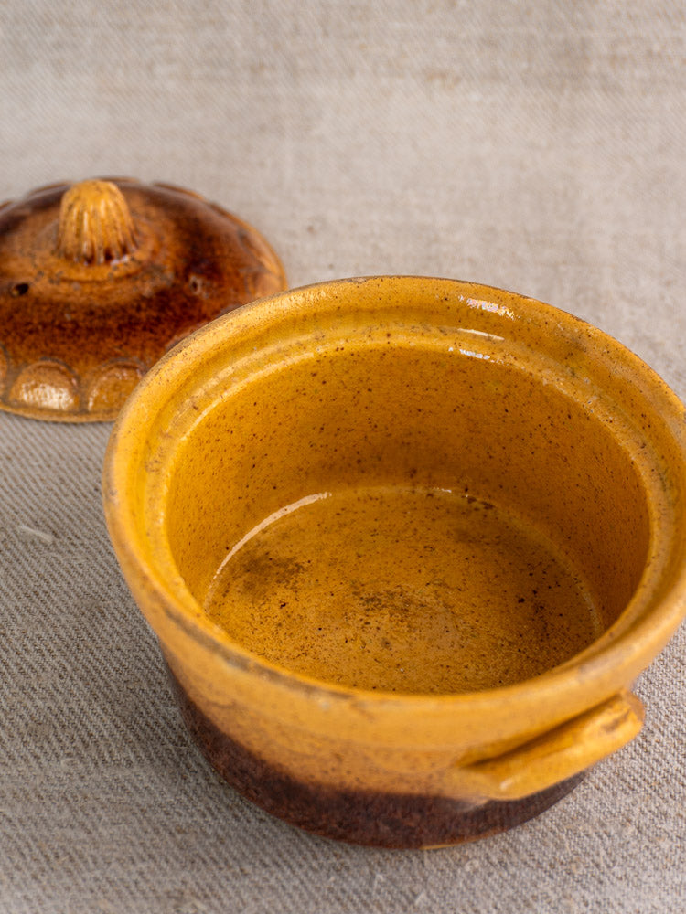 Antique French cocotte, small round yellow-brown Alsace glazed earthenware with lid, on beige fabric.
