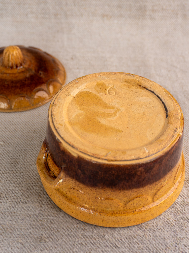 Antique French earthenware cocotte by Klein Strasbourg, upside down with lid beside, rustic Alsace glaze on beige textured surface.