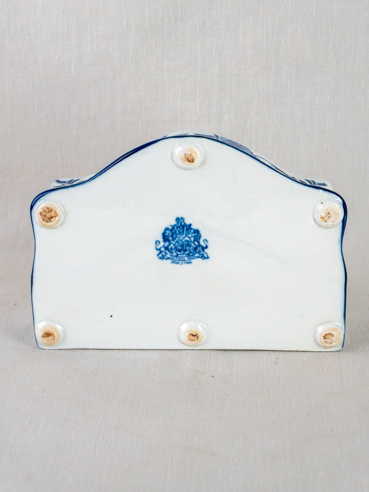 Underside of Blue and White Ironstone Inkstand with central blue crest and five unglazed spots, on textured fabric.