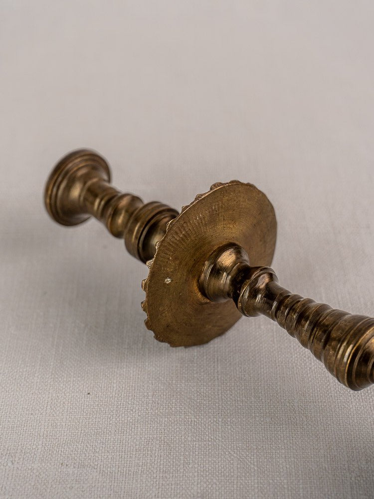 Antique French brass candlestick with scalloped mid-shaft drip pan on a lightly textured surface.